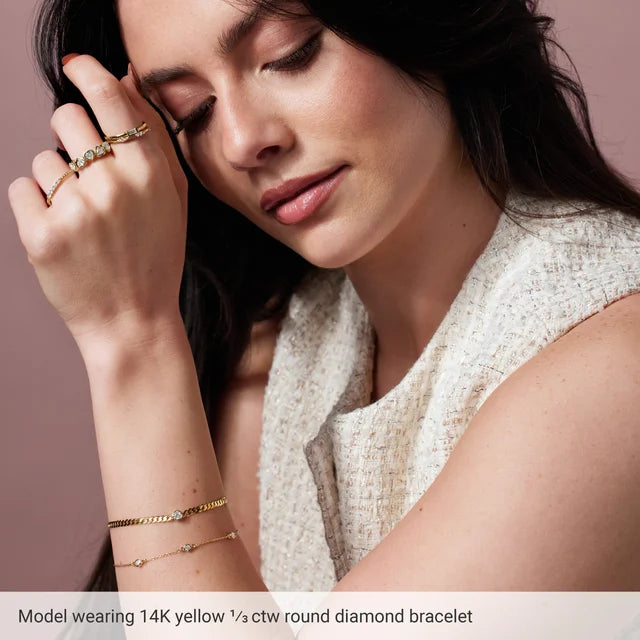 Woman wearing gold jewelry including a bracelet, ring, and necklace on a neutral background