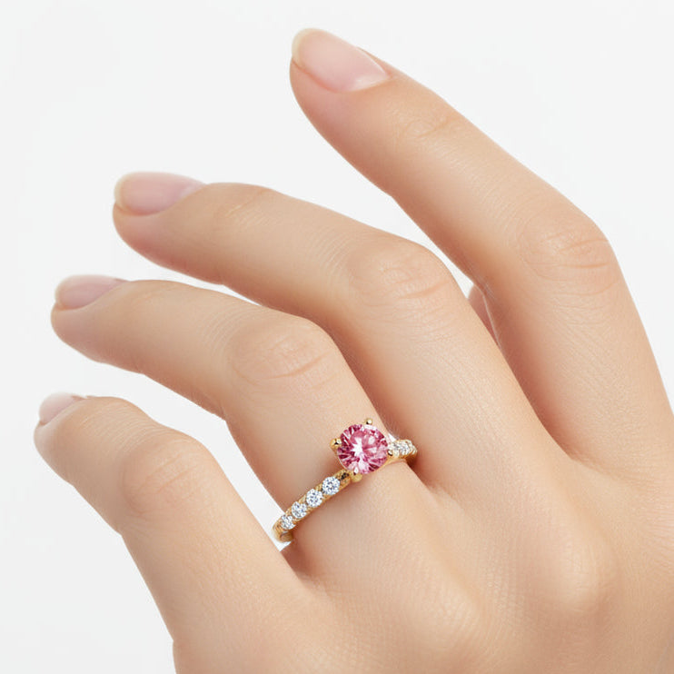 Gold ring with a red gemstone and diamond accents on a white background